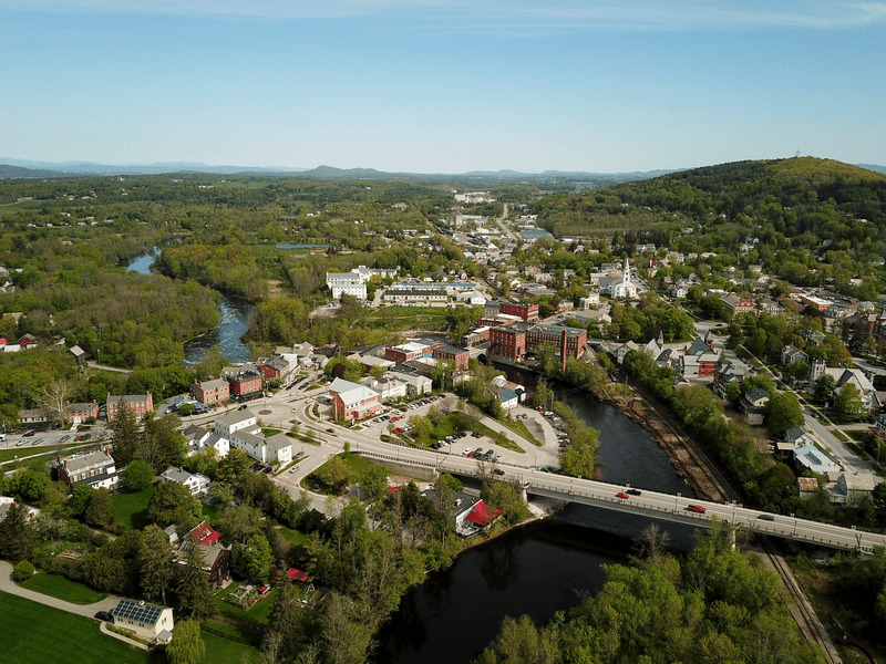 Seen from above, a rural town nestled among trees and a bridge spanning a river.