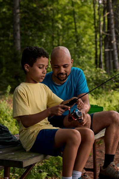 A parent shows a child how to use a fishing rod.