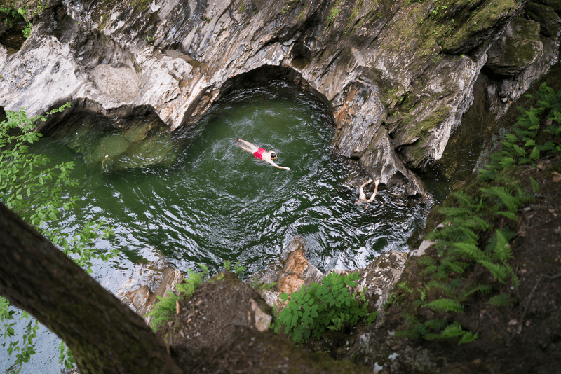 Seen from above, a person swims in a swimming hole in a forest.