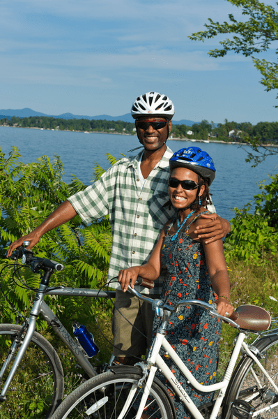Two people smile at the camera next to their bicycles and a large lake in the backgound.