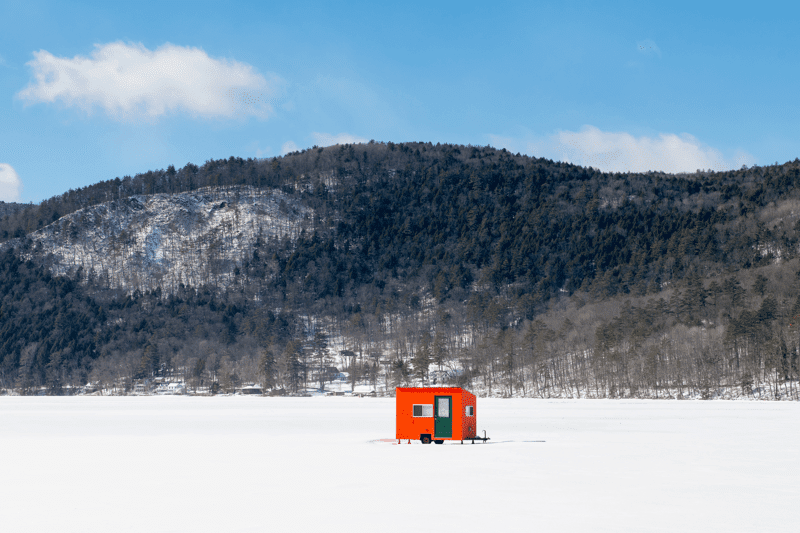 A red ice fishing shanty on a frozen lake in winter on a sunny day.