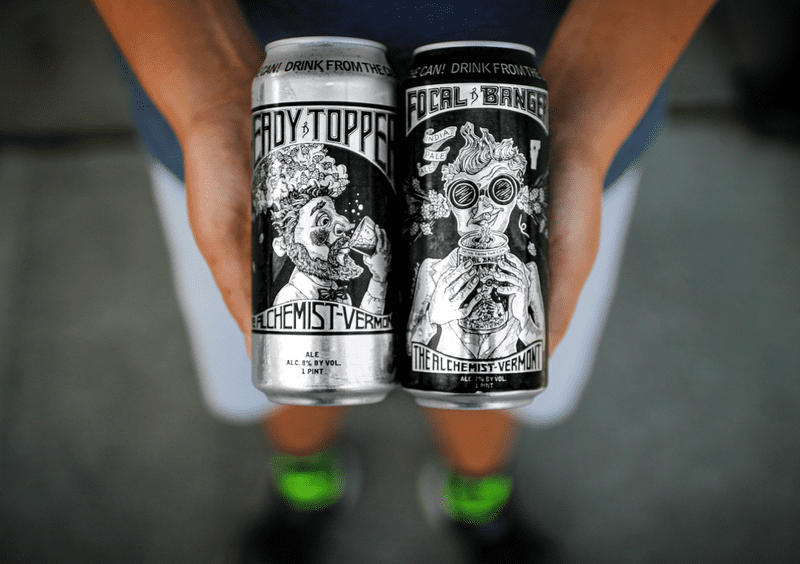 A creative product shot of the Alchemist's cans where a person holds a focal banger next to a heady topper.