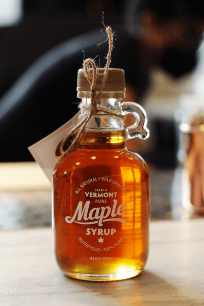 A small glass bottle of Vermont Maple Syrup illuminated by the sun.