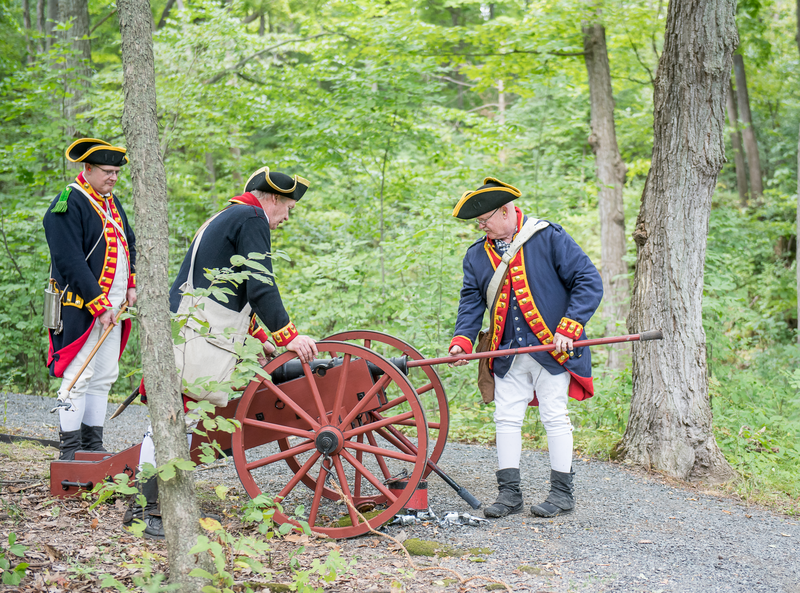 Three people dressed in 18th century outfits, load a canon.