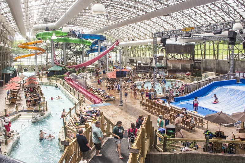 An indoor waterpark with multicolored slides and groups of people playing in a lazy river pool.