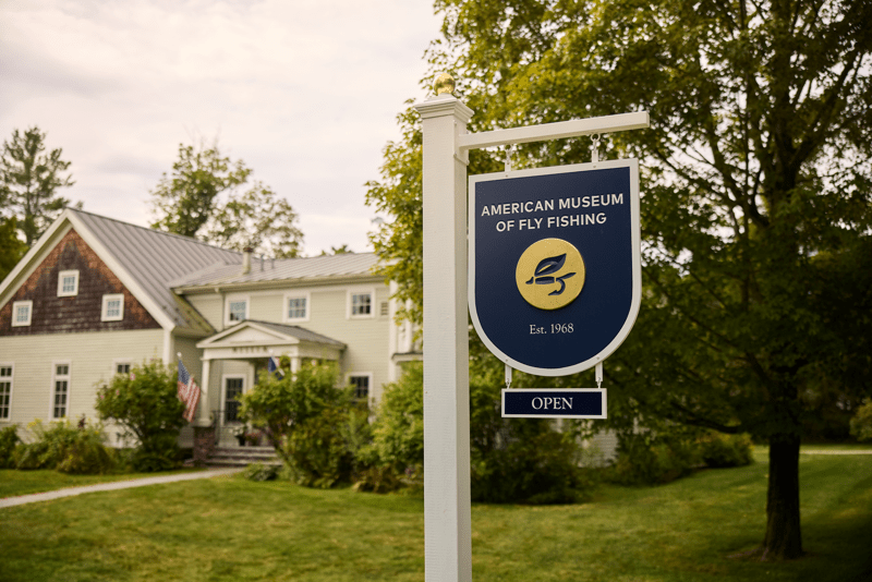 A sign reading “American Museum of Fly Fishing” seen exterior to a large building in the summer.