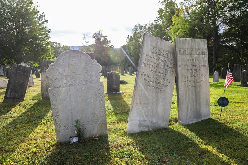 Three light grey tombstones in a cemetery on a sunny fall day.