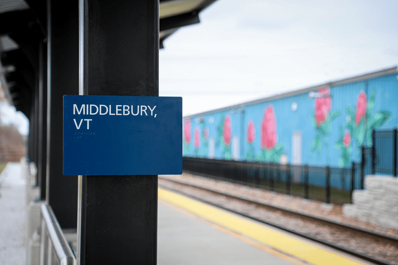 Signage at the Middlebury Amtrak Station with a mural of Red Clovers in the background.