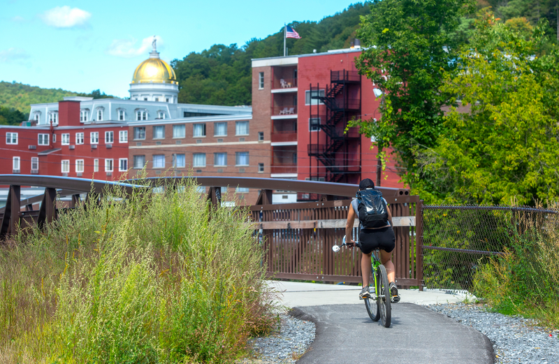 A biker approaches the bridge on Montpelier's bike path, with the golden dome in the background.