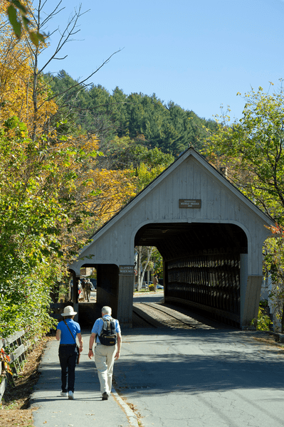 Pedestrians walk toward a covered bridge in the autumn.
