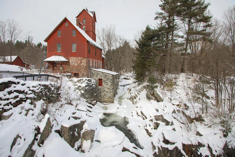 An old red barn is seen, from a distance, in the snow.