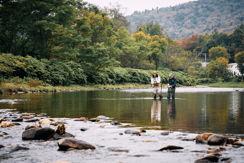 Two people discuss fly fishing standing in a river.