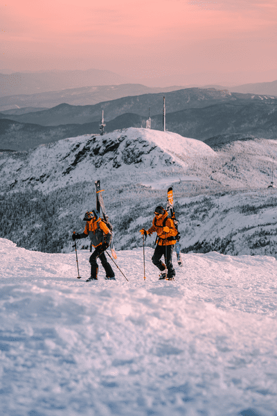 Two skiers hiking up Mount Mansfield during a pinkish hue.