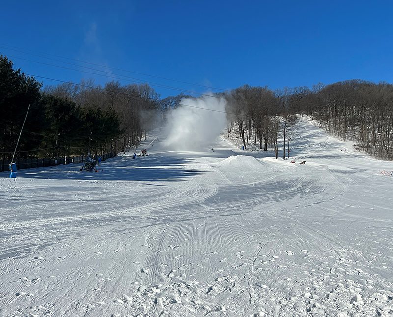 The view of a ski hill making snow, as powdery snow shoots into the air.