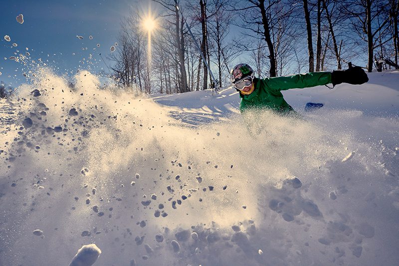 A person skis downhill and kicks up powder in front of the camera.