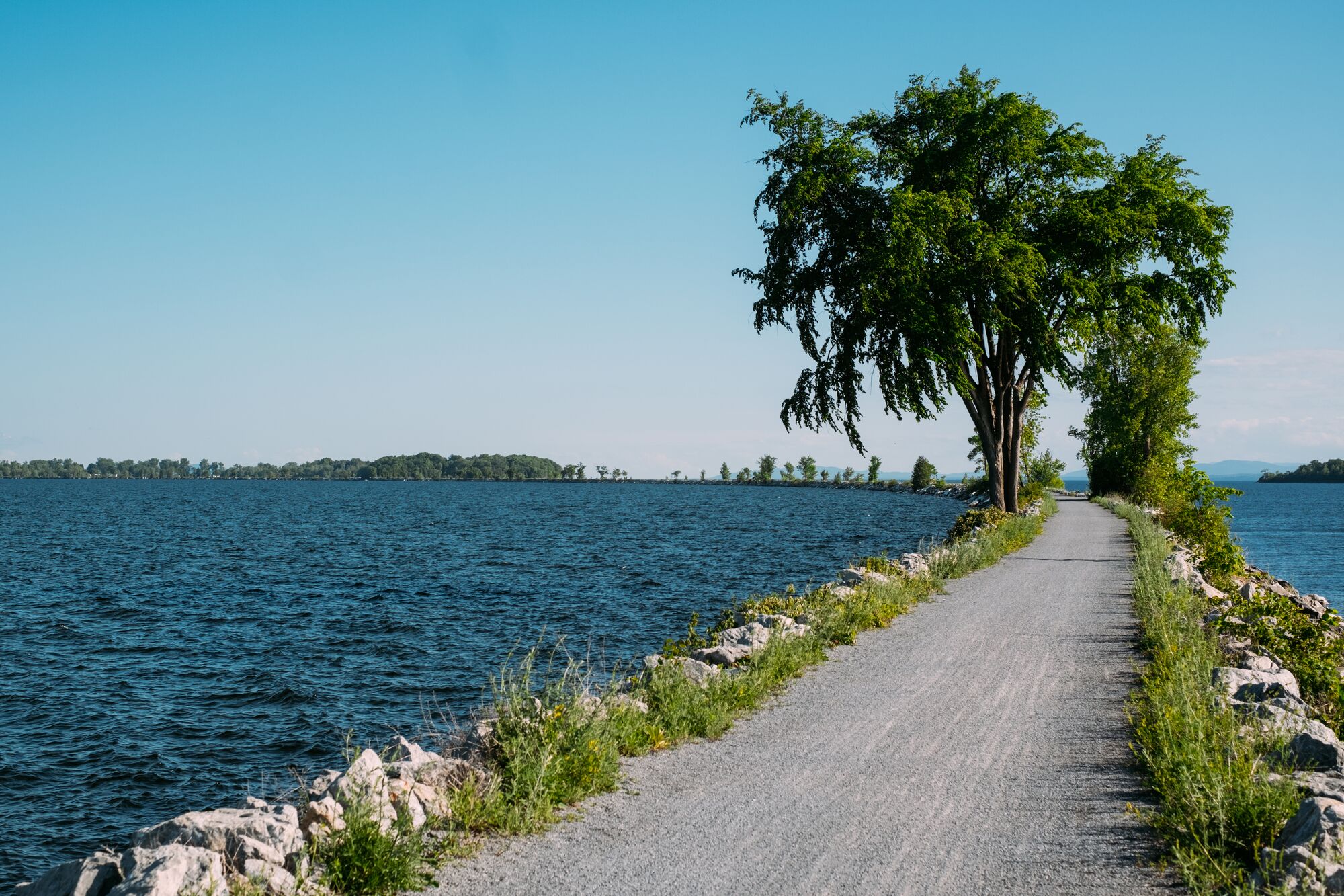 A gravel path on a blue lake outdoors on a sunny day.