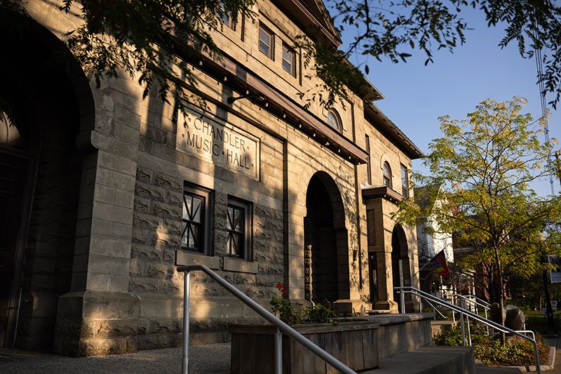 An old, stone building sits in the late day sun with the words Chandler Music Hall inscribed on the side.