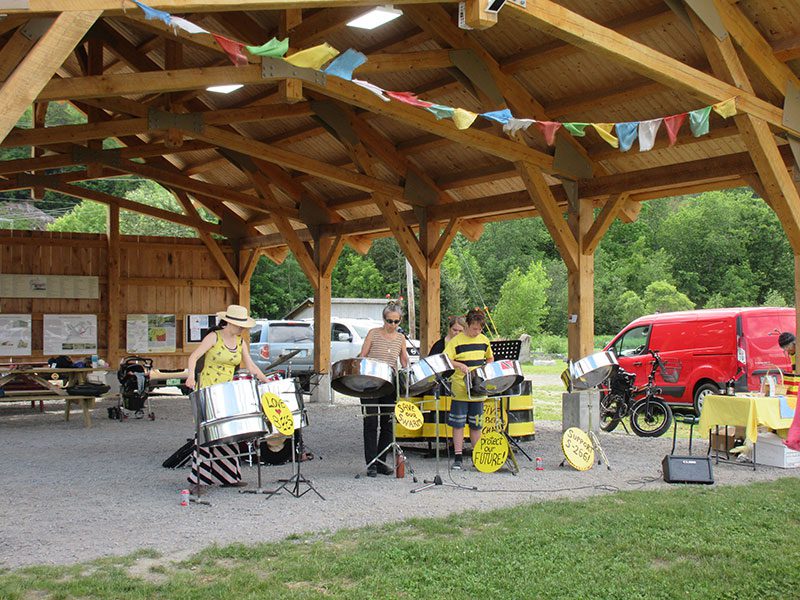 A small group of people play instruments under a wooden pavilion outside.