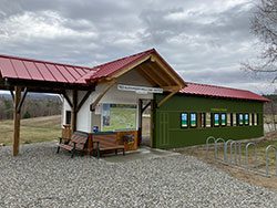 A sign reading Ted Alexander Welcome Center at a trailhead outside in the summer.