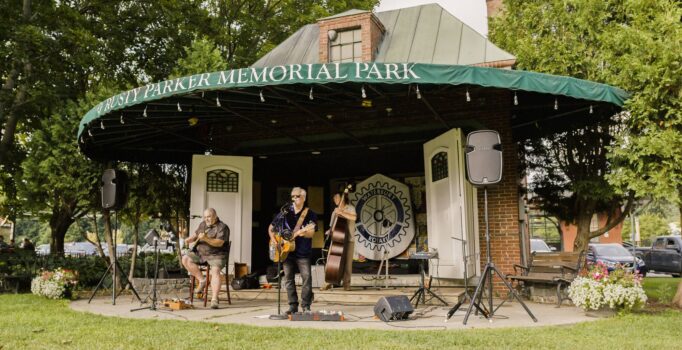 A group of musicians play live music in an outdoor park on a warm day.