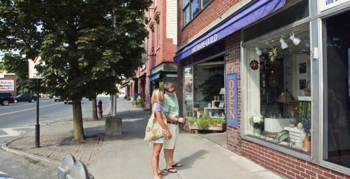 Two people window-shop in front of a storefront on a warm sunny day.