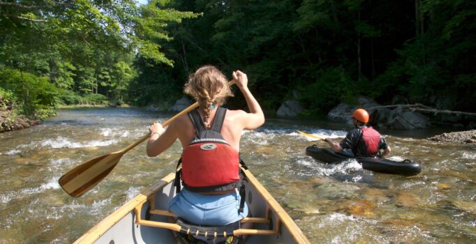 A canoe and a kayak paddle down a river.