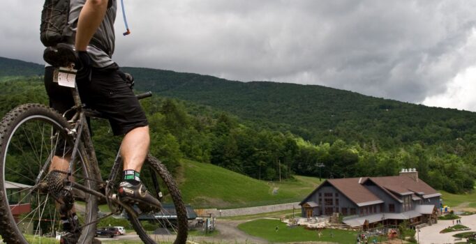 A person on a mountain bike pauses to look at the view of a building downhill.