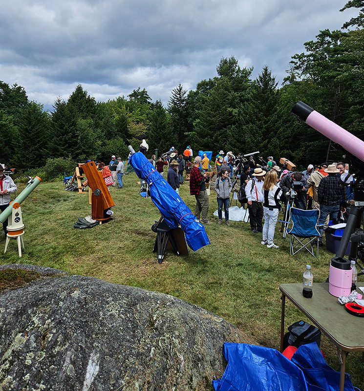 People gather around telescopes outdoors in the summer.