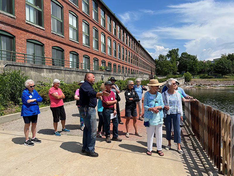 People tour outside of an old mill with a guide.