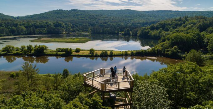 People stand on a wooden tower overlooking a body of water and forest.
