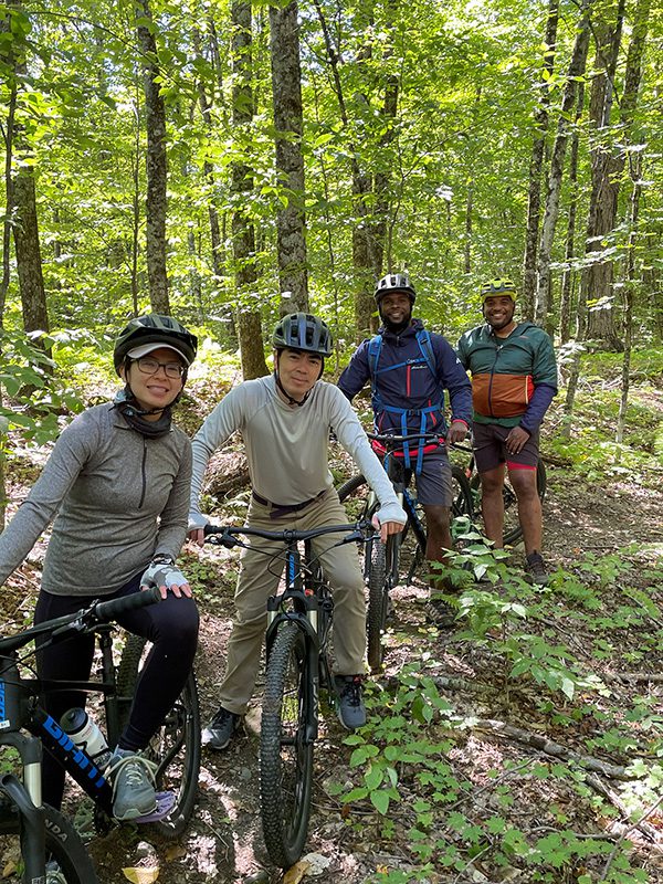 Four people on bikes in a forest smile for the camera.