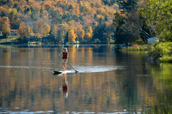 A person on a stand up paddle board paddles across a calm lake.