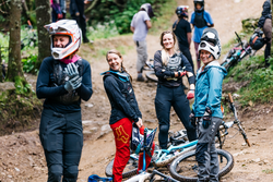 A group of people in mountain biking gear stand on a dirt trail with bikes laid on the ground.