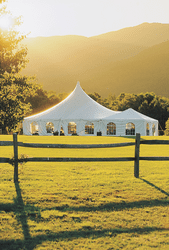 A large white event tent set up in a green field lit by sun.