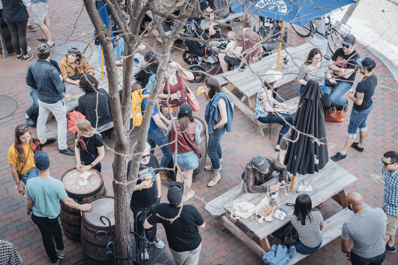 A photography from above, depicting a group of people enjoying picnic tables and conversation on a brick street in Winooski, Vermont.