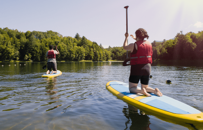 Two people paddleboard on a calm lake in the summer.