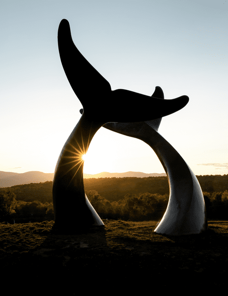 Two stone sculptures depicting whale tales are seen against the setting sun.