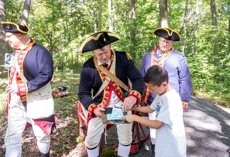 Man in period clothing shows a child a trail map of the property with two others standing behind.