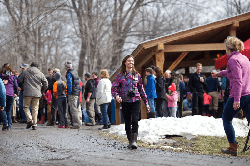 A spring scene of the Maple Season Opener focuses on an individual with a camera around their neck.