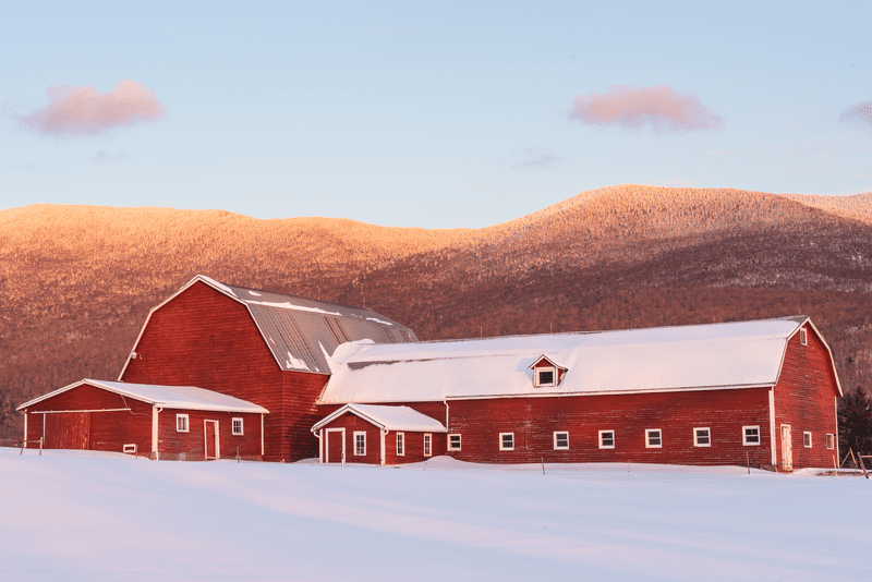 A red barn contrasts a blanket of snow in front of a beautiful mountain backdrop.