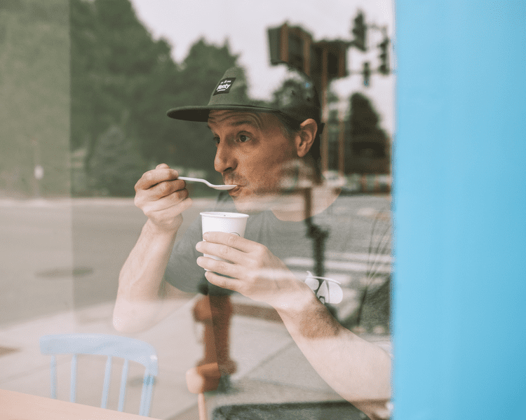 Dynamic image of a person eating ice cream through a window, which reflects the street scape behind.