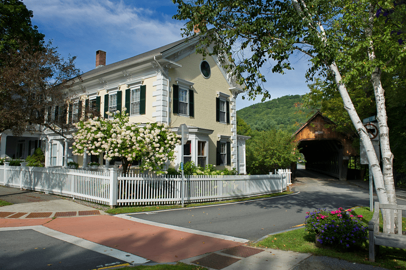 A Victorian-era home sits adjacent to a covered bridge.