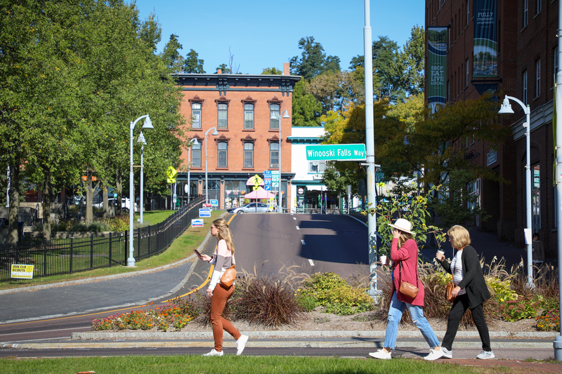 Three pedestrians walking along Winooski Falls Way, in Winooski, Vermont.