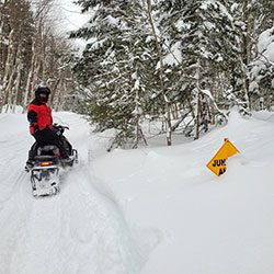 A person sitting on a stationary snowmobile turns back to look at the camera.