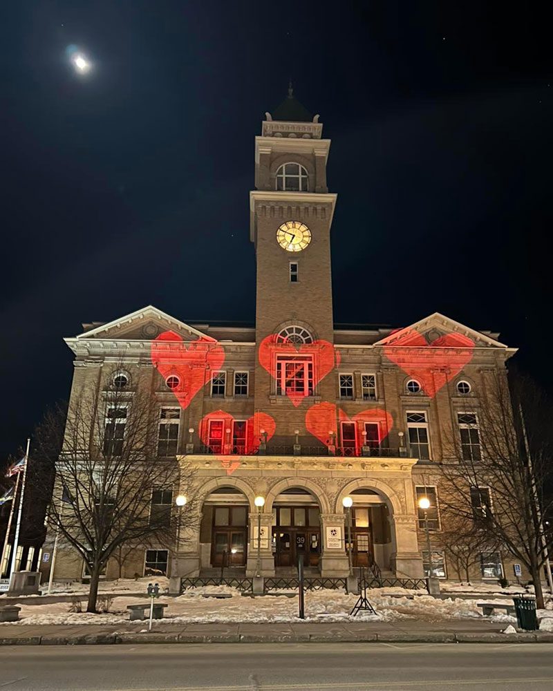 A large brick building is slit up with red hearts at night.