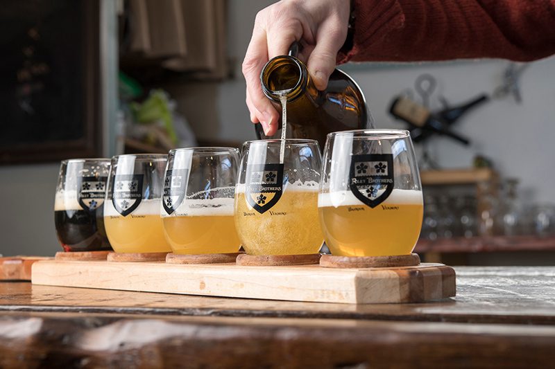 A person pours beer into a flight of beer glasses.