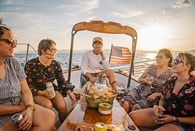 Five people sit and talk on a boat at sunset.