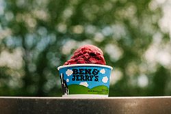 Bright red ice cream in a cup that reads Ben & Jerry’s on a wooden shelf.