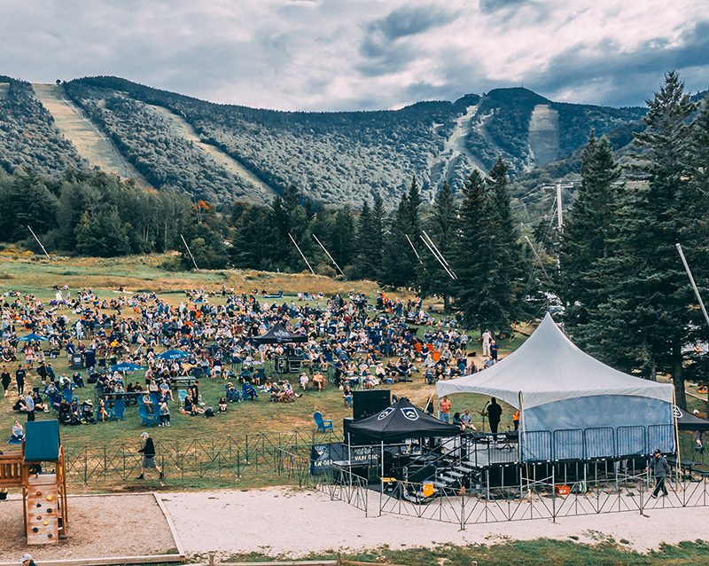 A crowd watches an outdoor concert on the lawn of a ski slope.