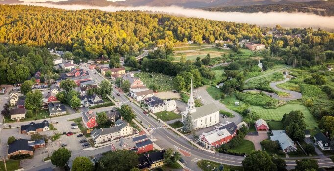 A town seen from above, with a white church in the town center and a mountain range in the background.